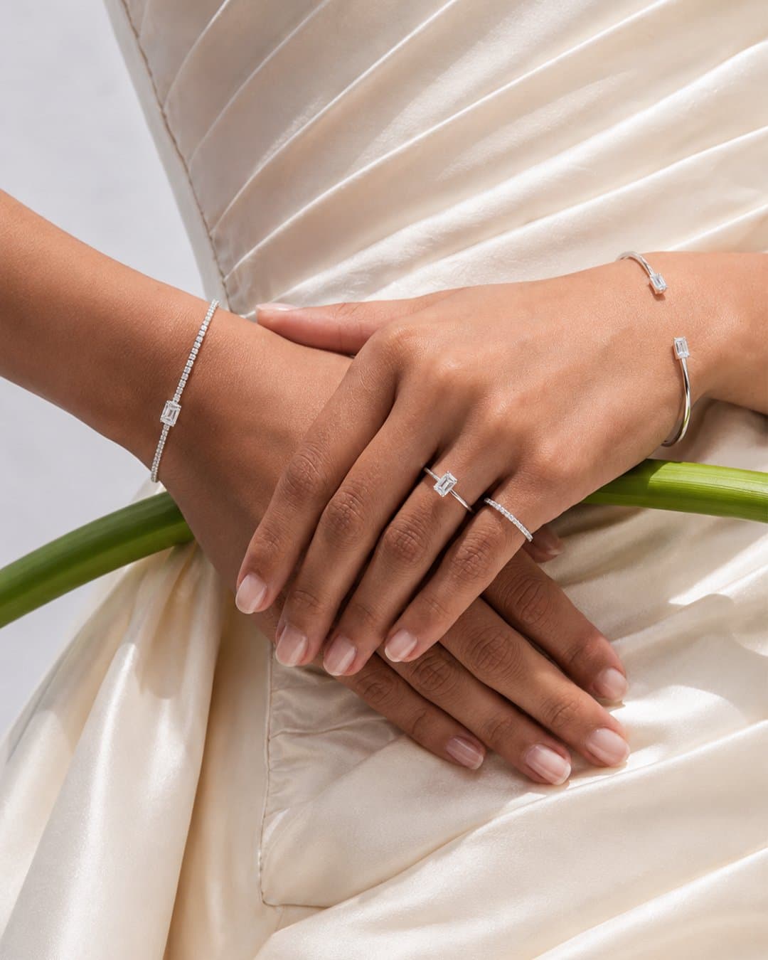 Hands resting on an ivory satin gown, wearing diamond bands and bracelets